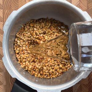 Water being added to soaked horse gram for curry in a steel pressure cooker