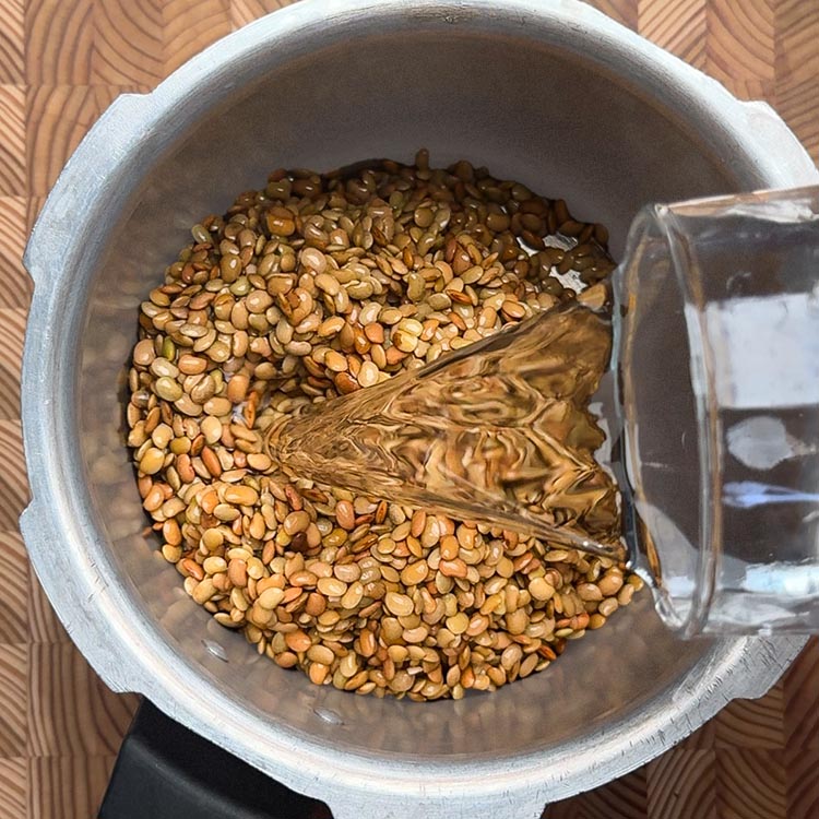 Water being added to soaked horse gram for curry in a steel pressure cooker