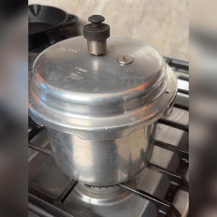 Closed pressure cooker on stove with steam releasing from valve