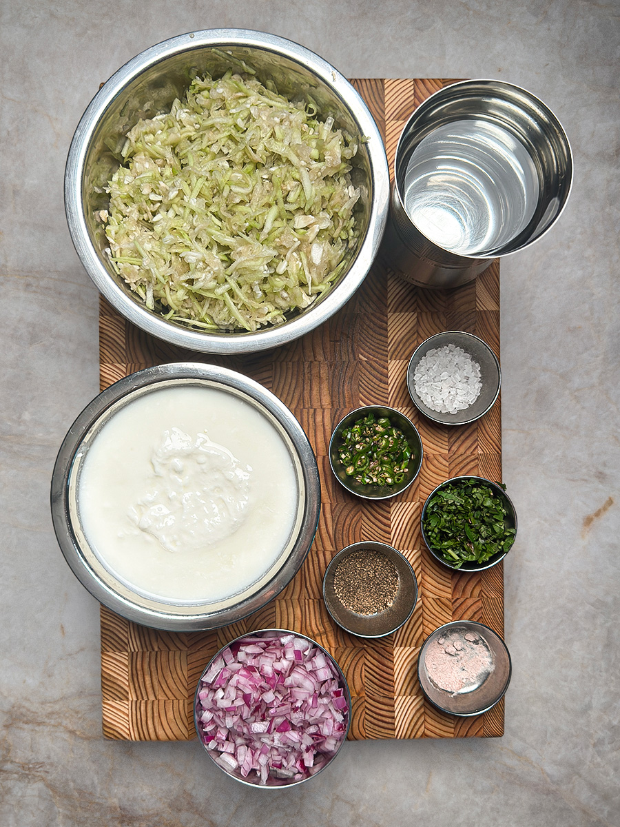 Fresh ingredients arranged on wooden cutting board including yogurt, grated vegetables, and Indian spices