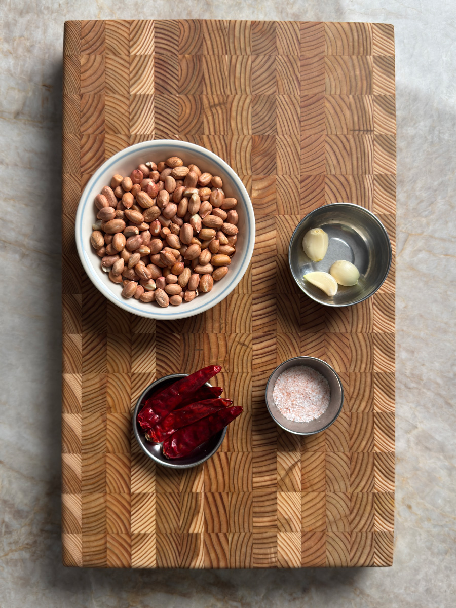 Raw peanuts, dried red chilies, garlic cloves and salt arranged on a wooden cutting board