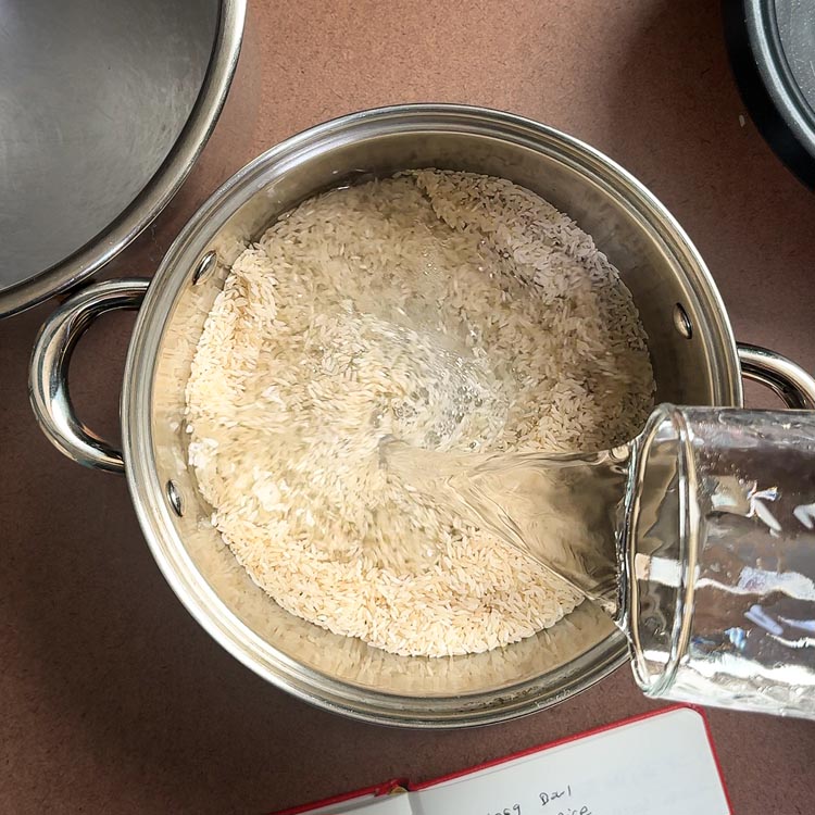 Clear water being poured over dry rice grains for rinsing