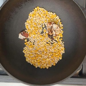 Light golden urad dal and chana dal roasting with small tamarind piece in black iron pan