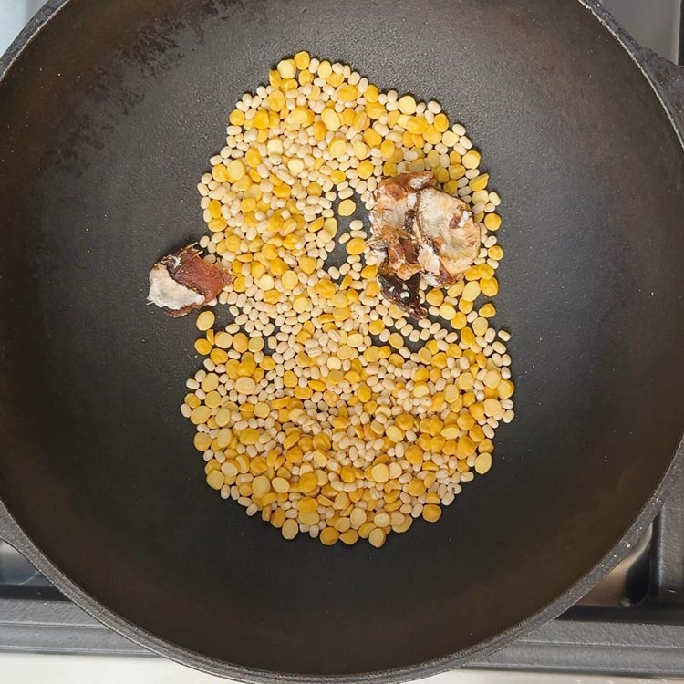Light golden urad dal and chana dal roasting with small tamarind piece in black iron pan
