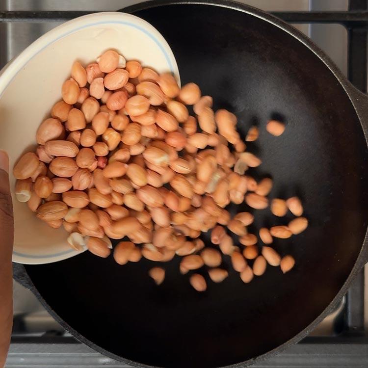 Raw peanuts being poured into a hot cast iron pan for dry roasting