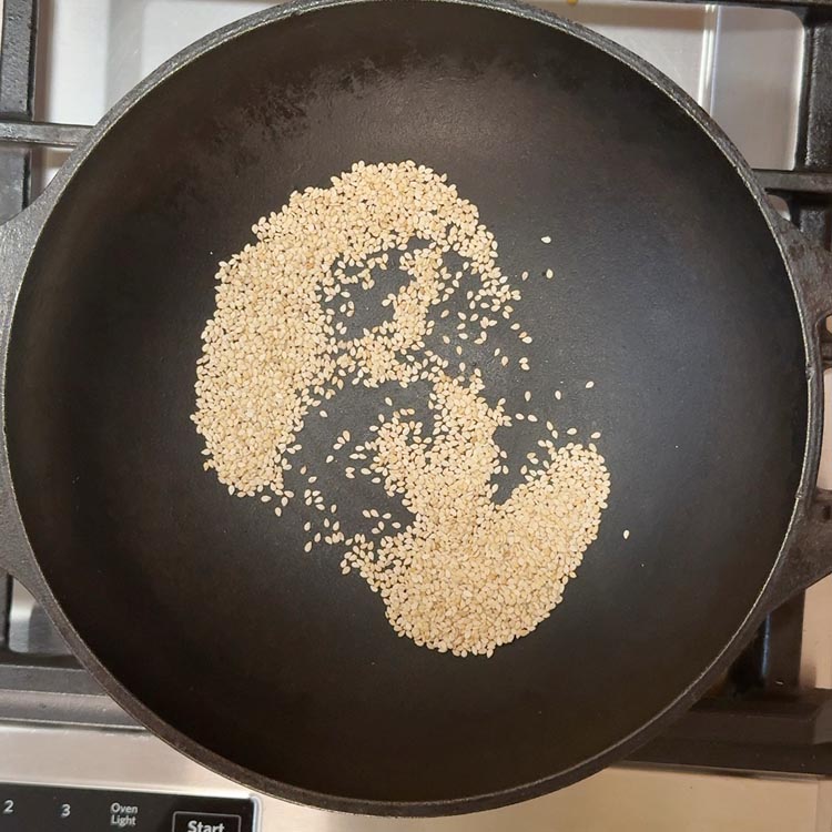 Golden sesame seeds roasting in a heavy-bottomed pan with visible steam rising