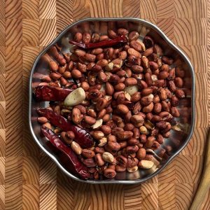 Salt being sprinkled over roasted peanuts, chilies and garlic mixture cooling on plate