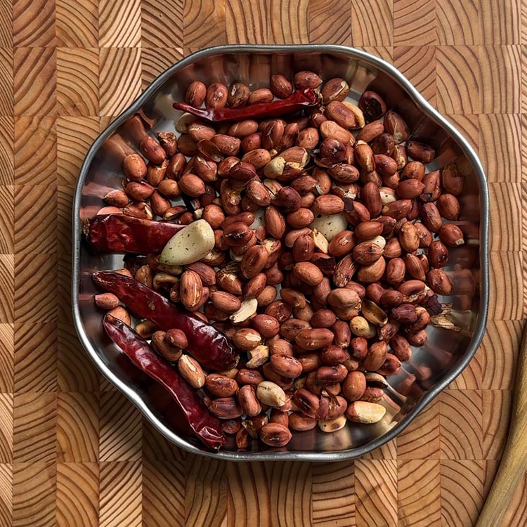 Salt being sprinkled over roasted peanuts, chilies and garlic mixture cooling on plate