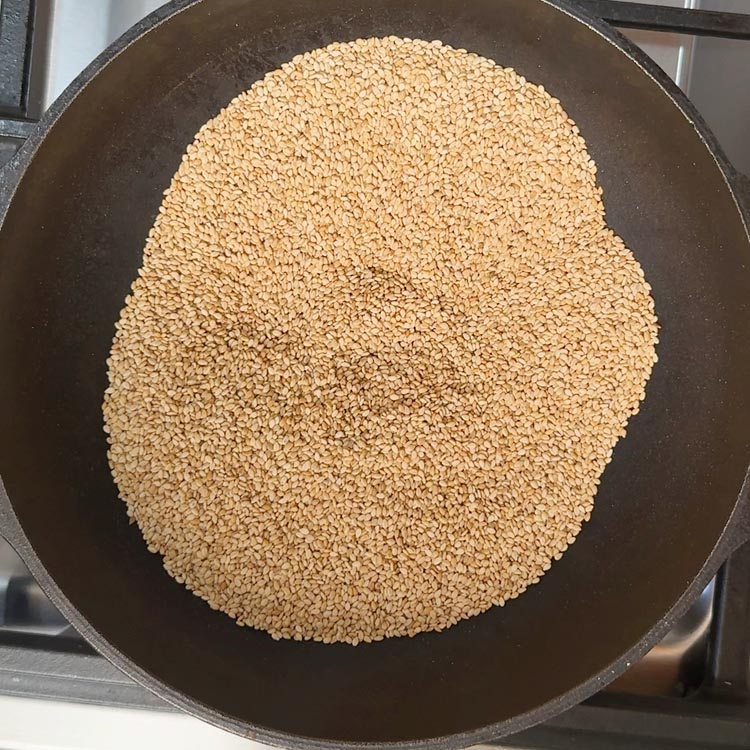 Golden sesame seeds roasting in heavy-bottomed pan with wooden spoon stirring