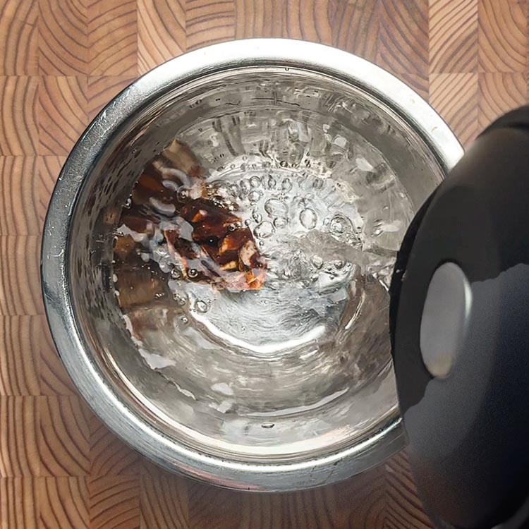 Warm water being poured over dark brown tamarind in a small bowl