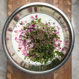 White yogurt with green herbs and spices ready to mix in glass bowl