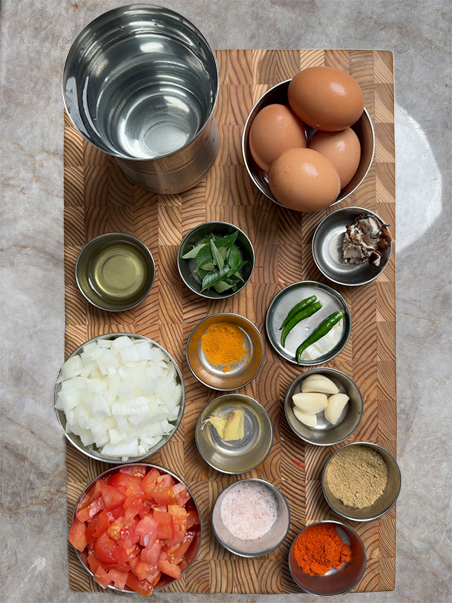 Various spices, chopped vegetables, and eggs arranged in small glass bowls on a wooden cutting board