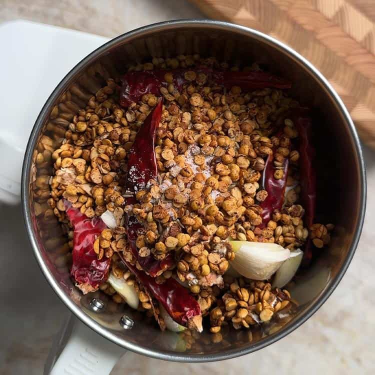 Roasted toor dal, spices, and salt loaded in steel spice grinder ready for grinding