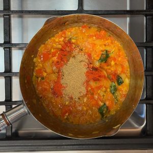 Red chili powder and brown coriander powder being stirred into the egg pulusu base