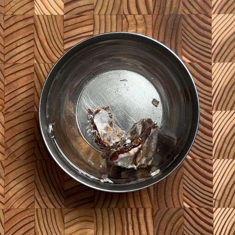 Dark brown tamarind pieces soaking in hot water in a small ceramic bowl