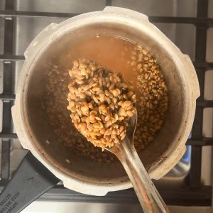 Spoon lifting soft cooked horse gram curry from pressure cooker