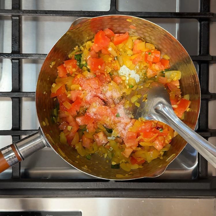 Chopped red tomatoes cooking down into a thick, chunky gravy base with steam rising