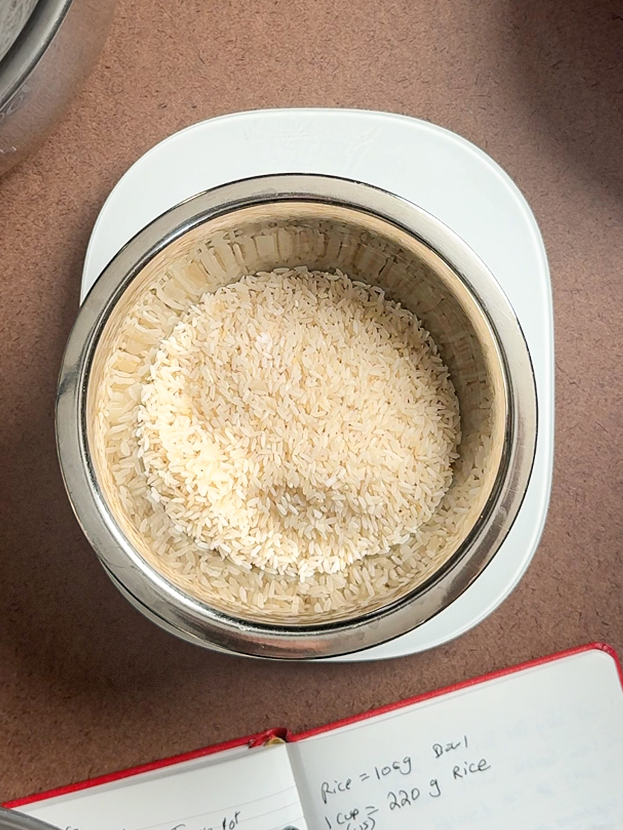 One cup of white rice measured into a bowl on a weighing scale