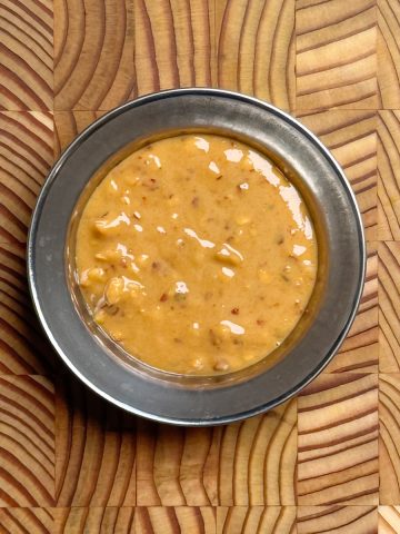 Creamy golden 5 minute spicy peanut dressing with visible red pepper flakes in a dark metal bowl on wooden surface