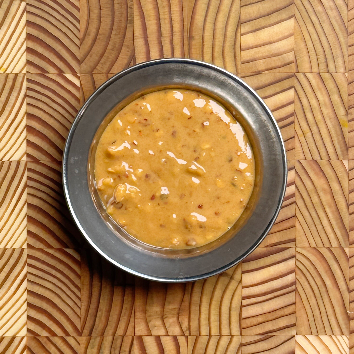 Creamy golden 5 minute spicy peanut dressing with visible red pepper flakes in a dark metal bowl on wooden surface