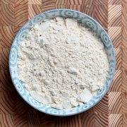 Creamy white Pappula Podi powder in decorative blue ceramic bowl on textured wooden surface
