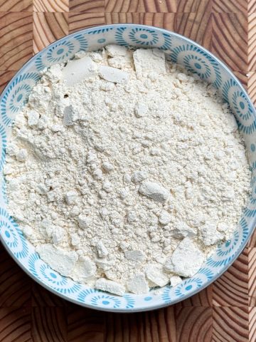 Creamy white Pappula Podi powder in decorative blue ceramic bowl on textured wooden surface
