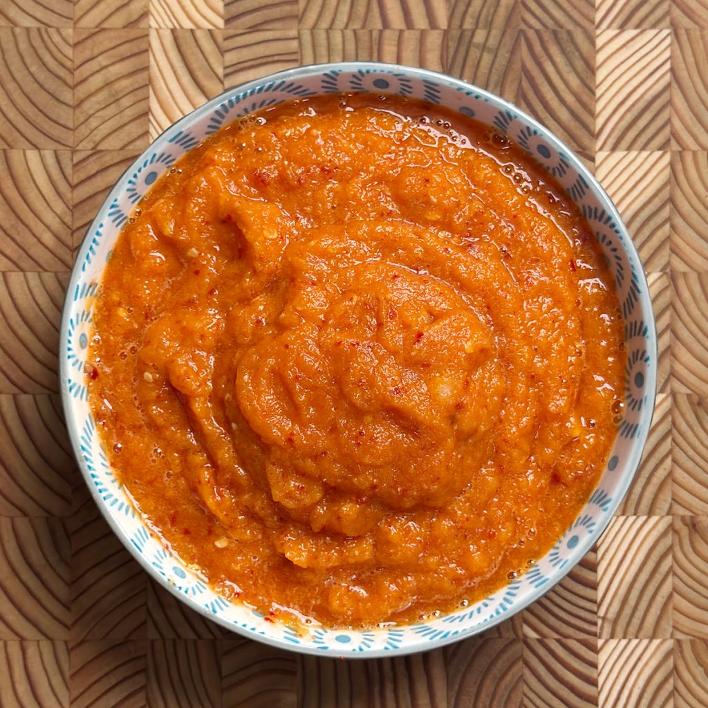 Vibrant orange-red Erra Karam with coarse texture served in traditional blue and white ceramic bowl on wooden surface