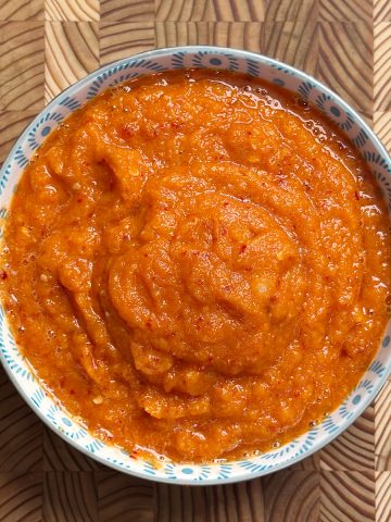 Vibrant orange-red Erra Karam with coarse texture served in traditional blue and white ceramic bowl on wooden surface
