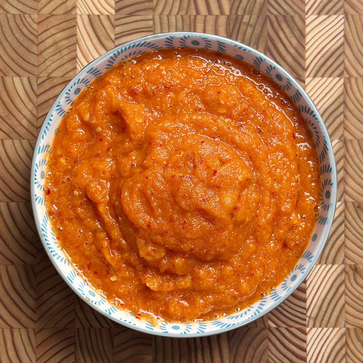 Vibrant orange-red Erra Karam with coarse texture served in traditional blue and white ceramic bowl on wooden surface