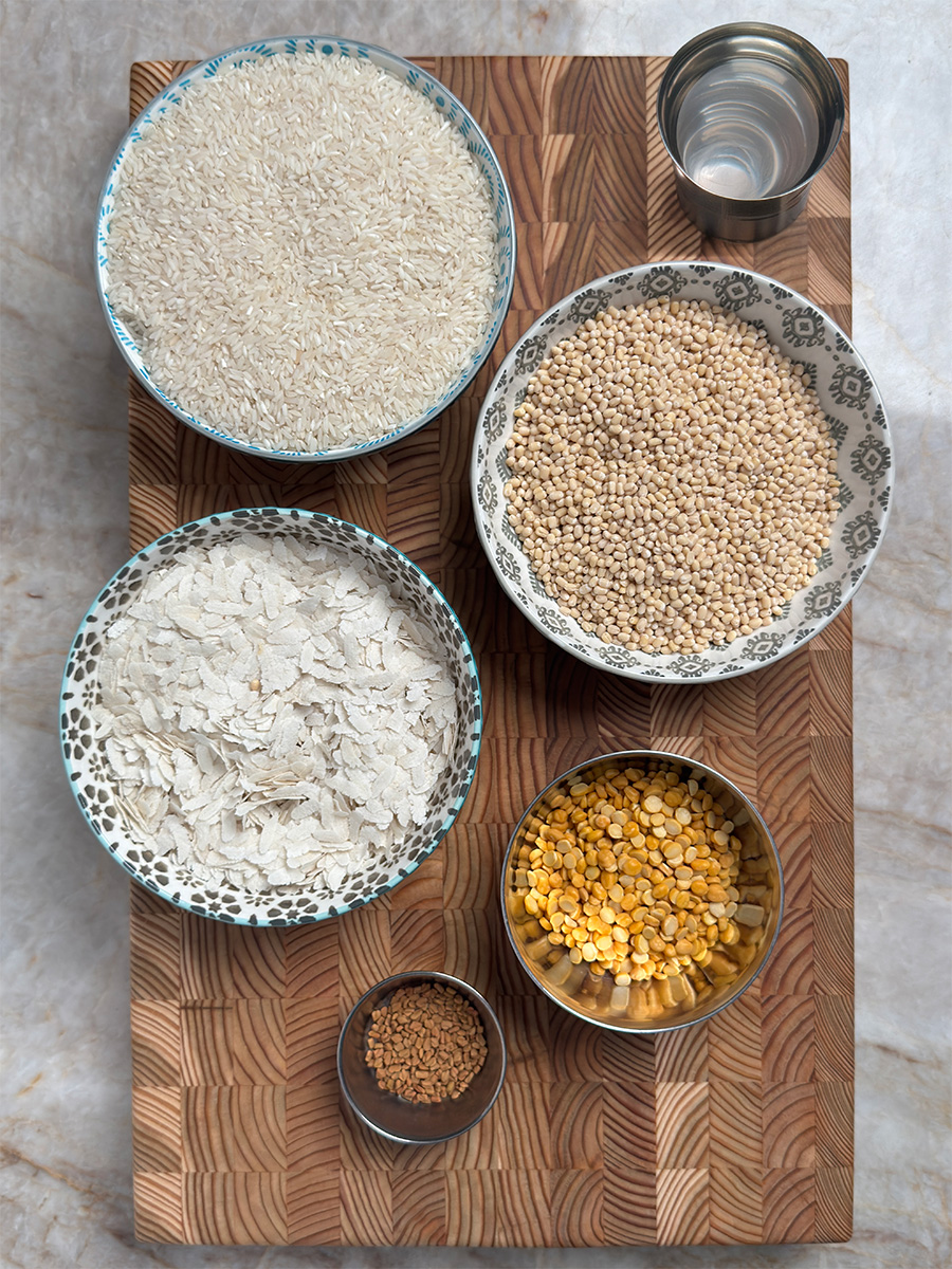 All ingredients for authentic Sona Masoori dosa batter - rice, urad dal, chana dal, poha, fenugreek seeds and water arranged on wooden board