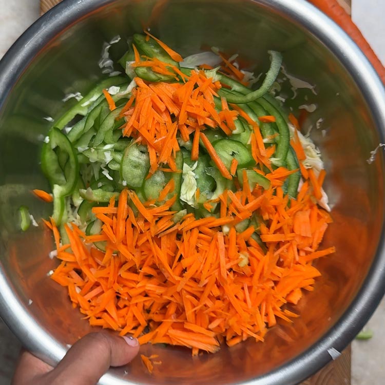 Colorful cabbage carrot green pepper salad base being combined in stainless steel mixing bowl