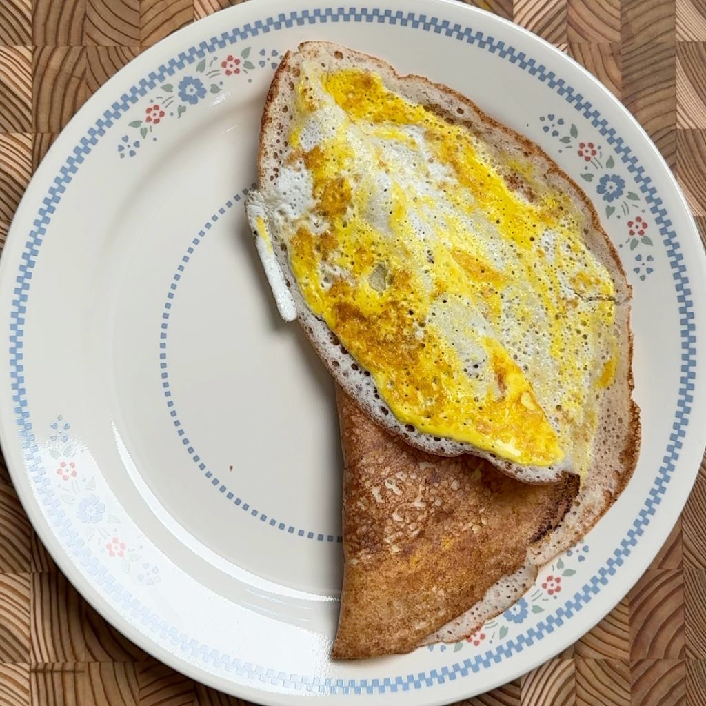 Golden brown easy egg dosa folded in half on decorative blue floral plate, showing crispy edges and egg filling