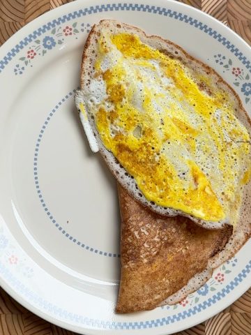 Golden brown easy egg dosa folded in half on decorative blue floral plate, showing crispy edges and egg filling
