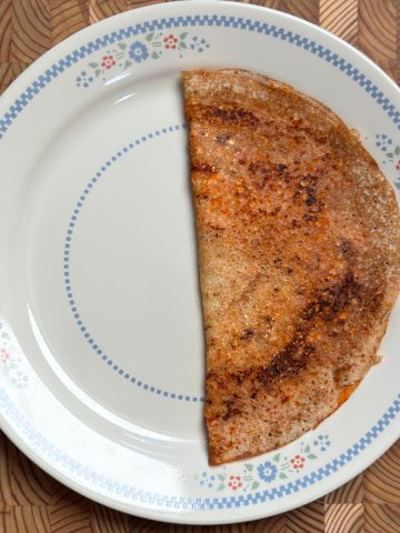 Golden crispy Erra Karam Dosa recipe folded in half on decorative white plate with blue floral rim