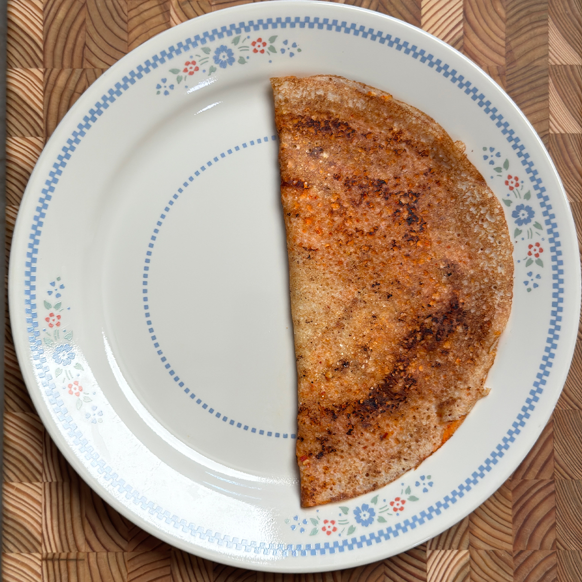 Golden crispy Erra Karam Dosa recipe folded in half on decorative white plate with blue floral rim