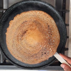 Steel spatula revealing golden brown cooked dosa with crispy texture after flipping from white side