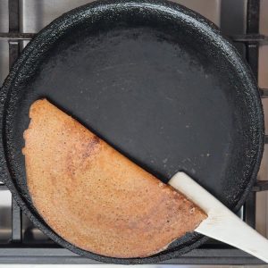 Steel spatula folding golden brown crispy crepe in half showing perfectly cooked texture