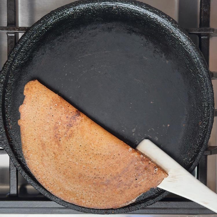Steel spatula folding golden brown crispy crepe in half showing perfectly cooked texture