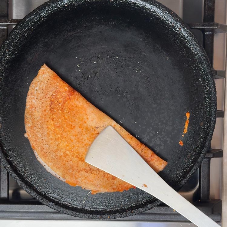Finished dosa being folded in half with spatula showing vibrant red and beige spice toppings
