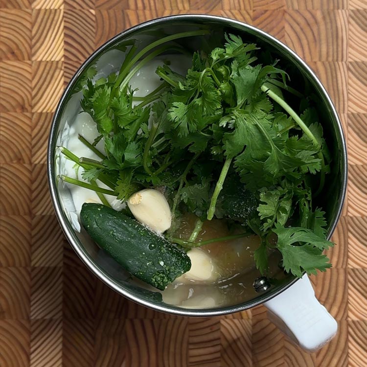 Fresh cilantro leaves, garlic cloves and jalapeño pepper in stainless steel food processor bowl before blending