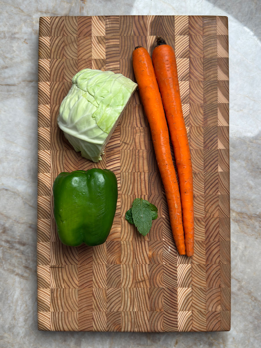 Fresh cabbage head, orange carrots, green bell pepper and mint leaves arranged on wooden cutting board