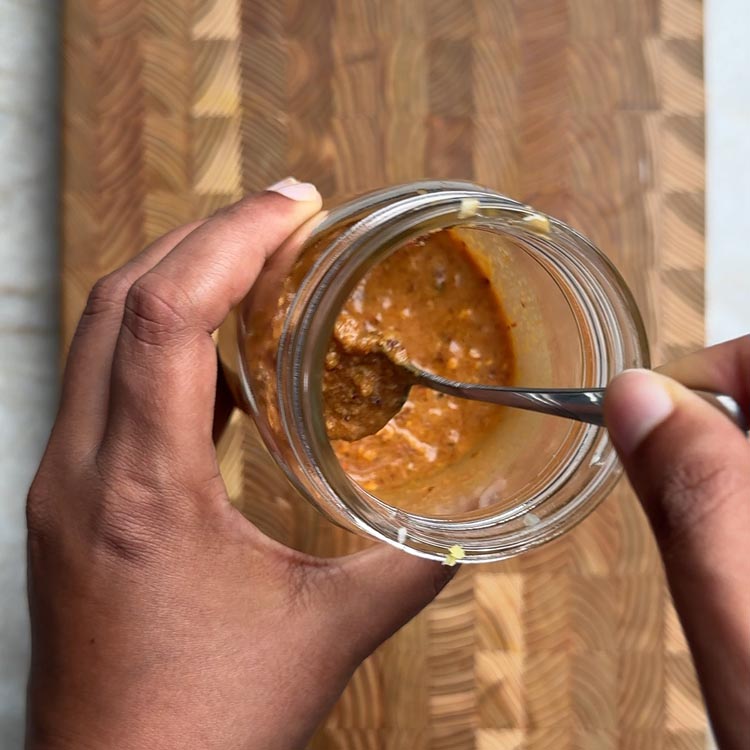 Hands holding glass jar filled with golden peanut dressing, showing creamy consistency perfect for salads and bowls