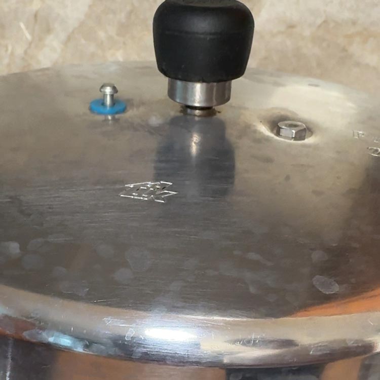 White steam escaping from pressure release valve on aluminum pressure cooker lid