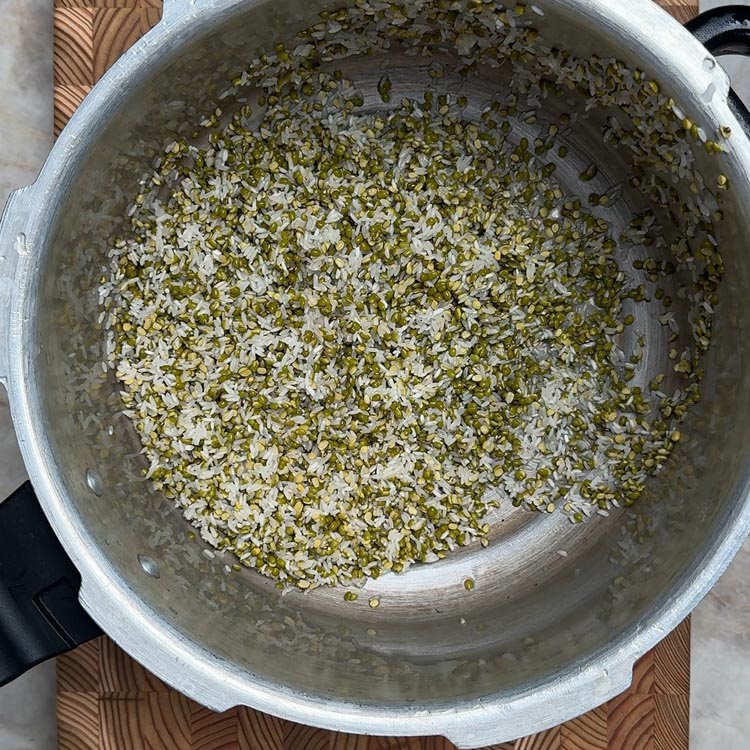 Clean rice and moong dal grains floating in clear water after rinsing in pressure cooker