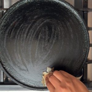 Hand rubbing a cut onion piece on hot cast iron tawa surface to prevent sticking