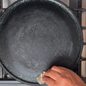 Hand rubbing half onion across hot black cast iron tawa to create non-stick surface for cooking