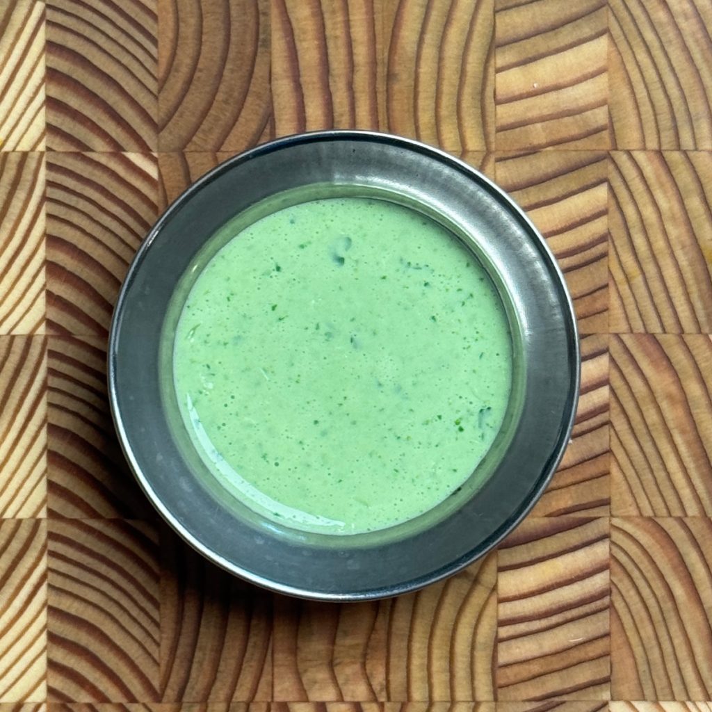 Smooth, vibrant green yogurt dressing with visible herb flecks in dark metal bowl showing creamy consistency