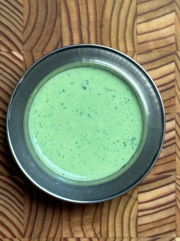 Smooth, vibrant green yogurt dressing with visible herb flecks in dark metal bowl showing creamy consistency