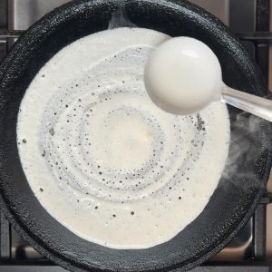 Steel ladle spreading white batter in spiral motion from center outward creating thin even layer