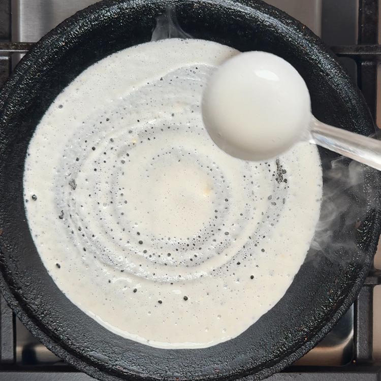 Steel ladle spreading white batter in spiral motion from center outward creating thin even layer
